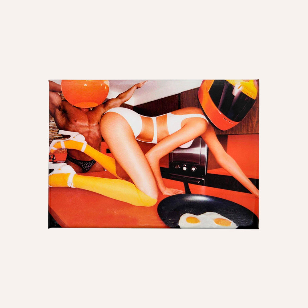 Magnet showing a person in white underwear lying on a red surface with an orange bowl and yellow socks.