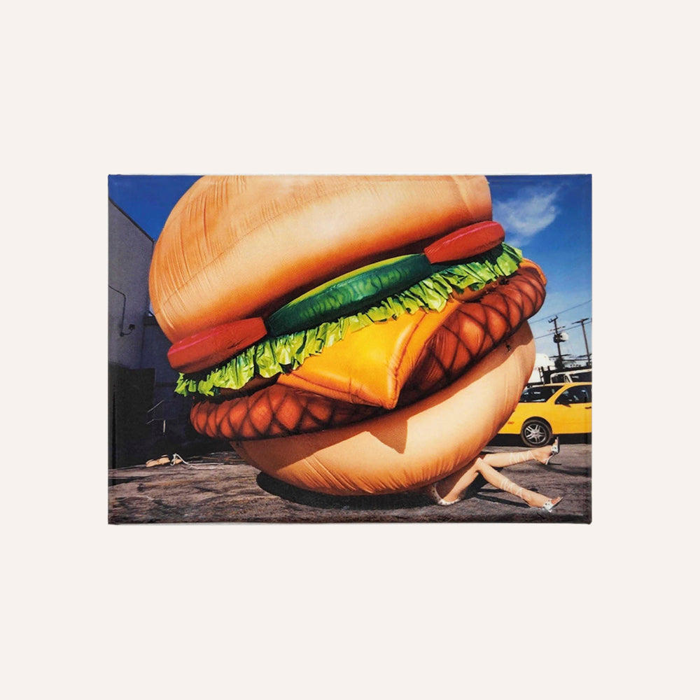 Magnet showing motif of an inflatable burger on a city street with a yellow taxi in the background