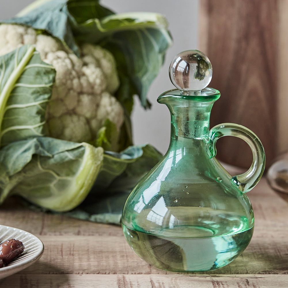 Green glass decanter on a wooden table with cauliflower in the background