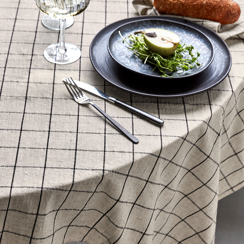 Dinner setting with a plate of food, cutlery, and a glass on a checkered tablecloth.