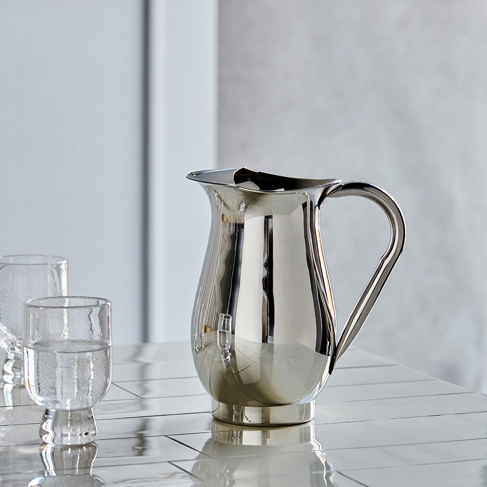 Silver pitcher and glasses on a reflective surface