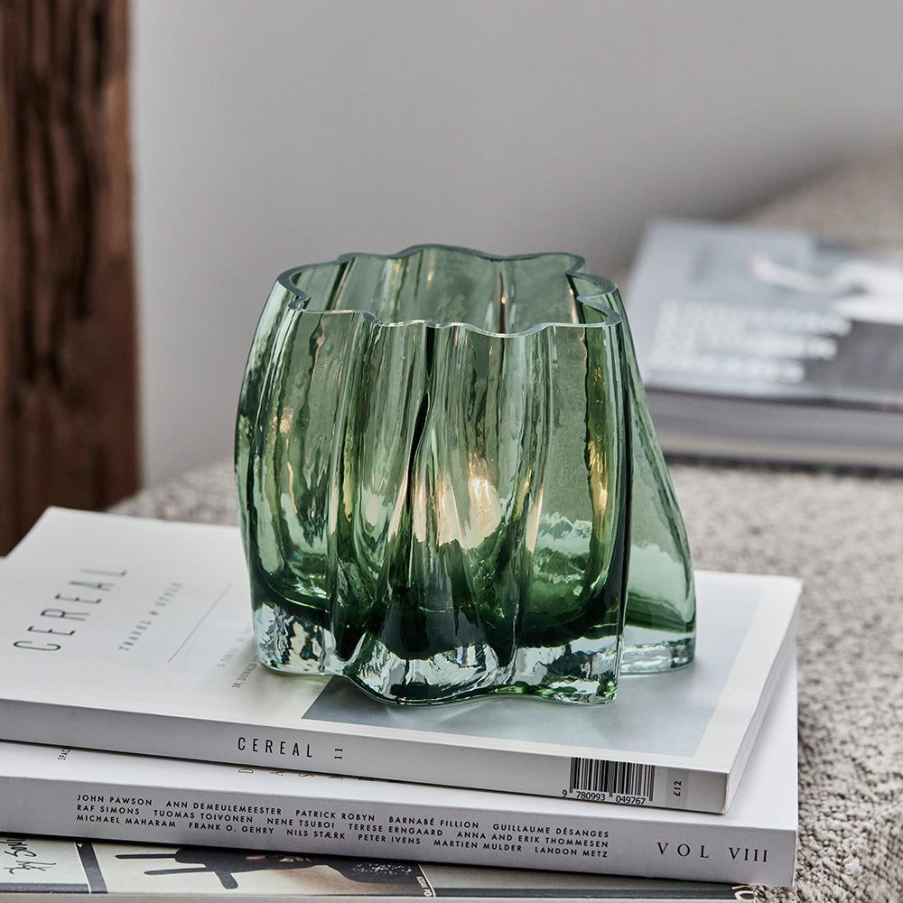 Green glass candle holder on a stack of books with a blurred background