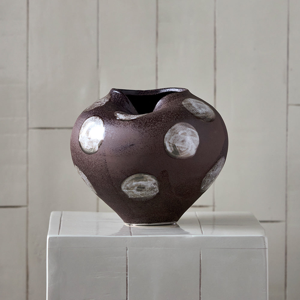 Brown ceramic vase with white circular accents on a white pedestal 
