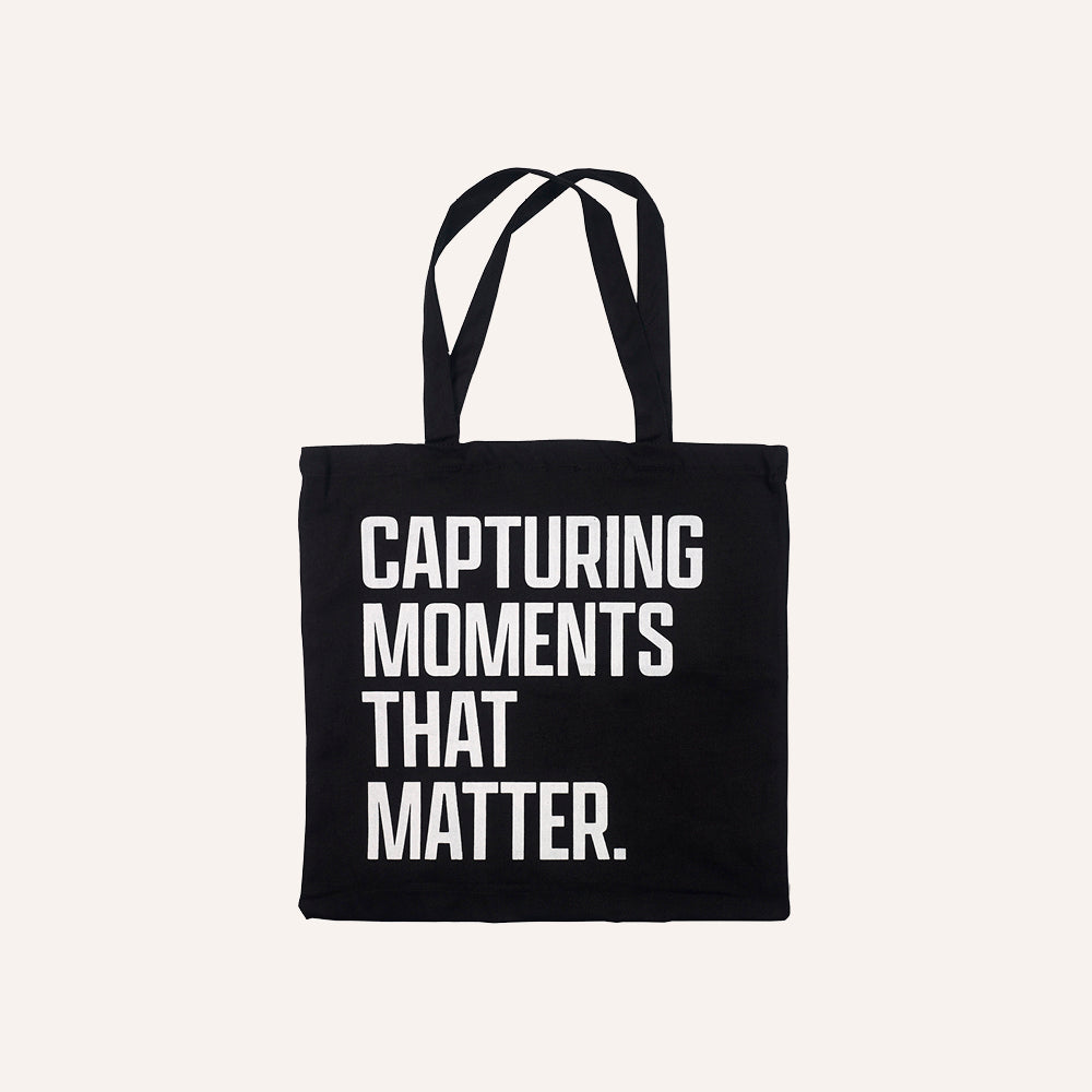 Black tote bag with white text 'CAPTURING MOMENTS THAT MATTER' 