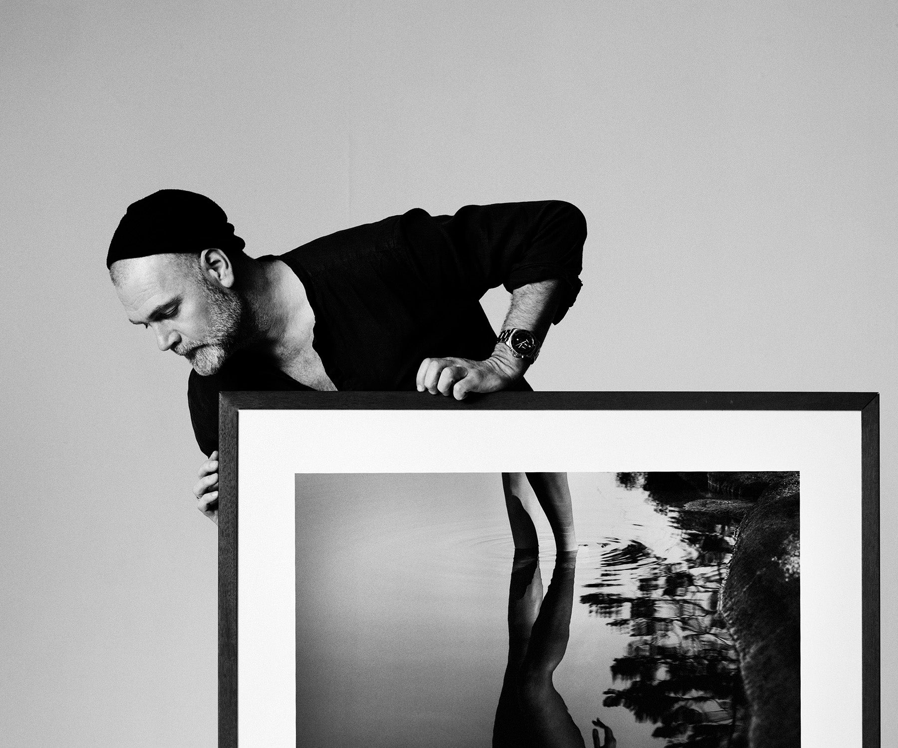 Man holding a framed black and white photograph of a person by water